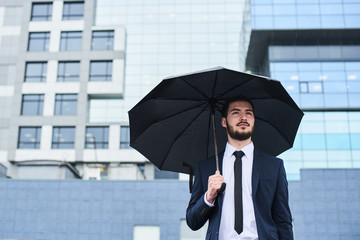 Guy in suit with umbrella in hands on background of building with glass facade