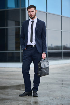 Portrait of a guy in a suit with a briefcase in hand on background of the building with a glass facade