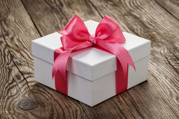 White gift box with a pink ribbon on the old board