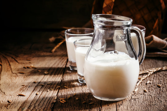 Fresh cow's milk in glass jug, vintage wooden background, still