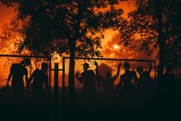 Several zombie behind a mesh fence at night.