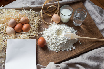 Flour, eggs and sheet of recipe on a wooden board