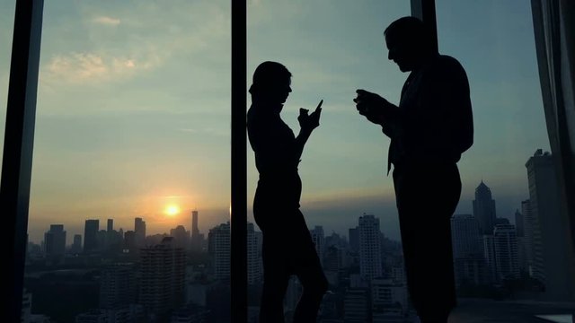 Businesspeople with smartphone standing by window in office
