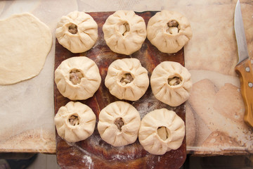Fototapeta premium Vak belyash - homemade meat pies on woden chopping board frosted with flour, near bread knife and pastry on table