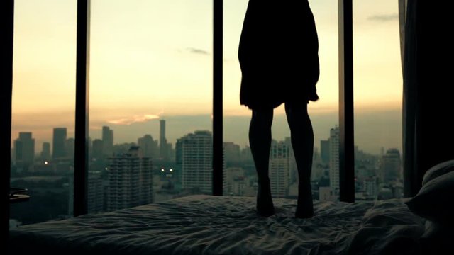 Happy woman jumping on bed in luxury apartment, super slow motion, 240fps
