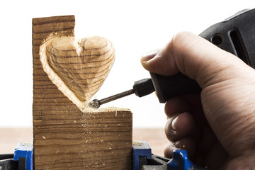 Carving wood in heart shape with rotary tool, on white background