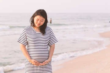Fototapeta premium Pregnant woman holding her belly on the beach with copy space in vintage tone.