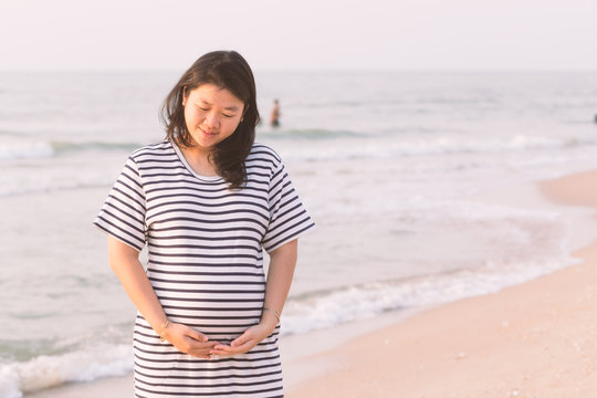 Pregnant woman holding her belly on the beach with copy space in vintage tone.