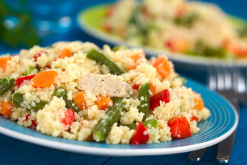 Couscous dish with chicken, green bean, carrot and red bell pepper served on plate with fork on the side (Selective Focus, Focus on the meat one third into the dish)