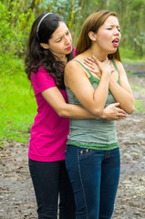 Young woman choking with lady standing behind performing heimlich maneuver, park environment and casual clothes