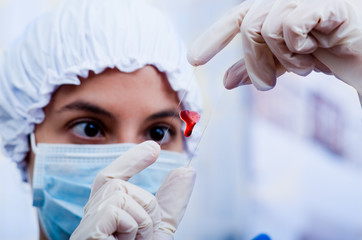 Closeup headshot nurse wearing bouffant cap and facial mask holding up blood sample on slide glass for camera