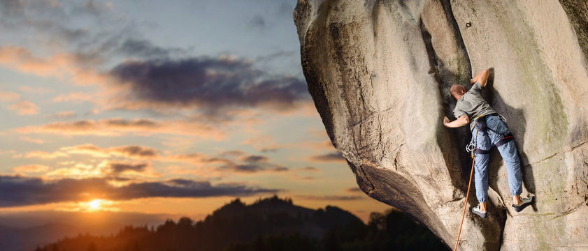 Young male rock climber climbing challenging route on rocky wall against scenic sunset background. Summer time. Climbing equipment. Panoramic image