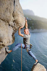 Side view of courageous man rock climber making difficult move up on overhanging cliff against...