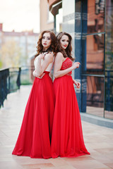 Portrait of two fashionable girls at red evening dress posed bac