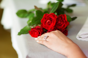 a female hand with a wedding ring lies next to red roses