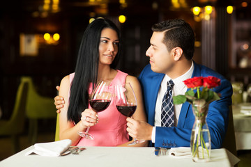 Beautiful young couple with glasses of red wine in luxury restaurant