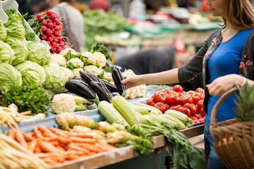 Young woman buying vegetable on stall.