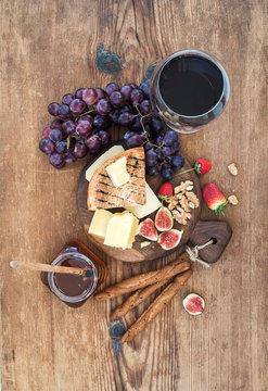 Glass of red wine, cheese board, grapes,fig, strawberries, honey and bread sticks  on rustic wooden table