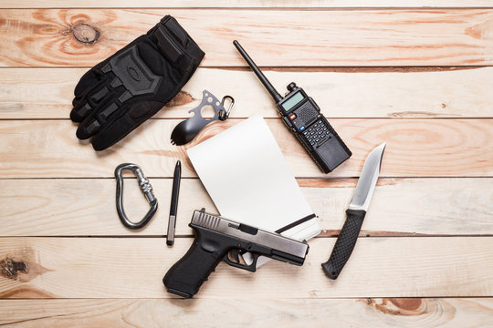 Assault rifle, gun, knife with sheath, compass and notebook with pen on table.