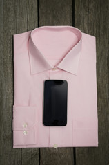 Pink shirt and mobile on wooden background