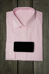 Pink shirt and mobile on wooden background