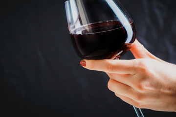 Hand holding glass of red wine on dark grey background