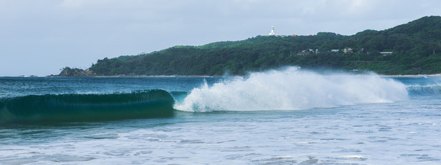 Byron Bay beach and waves in New South Wales, Australia with Cape Byron lighthouse in the...