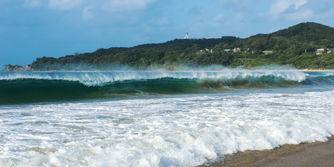 Byron Bay beach and waves in New South Wales, Australia with Cape Byron lighthouse in the background.