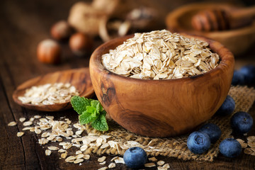 Rolled oats in a wooden bowl with fresh blueberries, sprig of mint and honey at the background