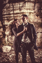 Fototapeta na wymiar Couple of well dressed peolpe on the dark rocks background.