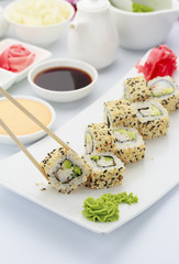 Japanese cuisine. Shrimp sushi roll ith sauces ginger and wasabi on a hite plate.