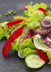 Salad with octopus baby corn and vegetables on a stone plate