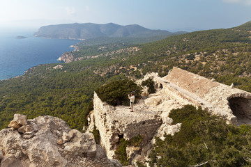 Fototapeta premium MONOLITHOS, RHODES, GREECE - September 14, 2015: A tourist photographs the sea coast panorama from the walls of the medieval castle of Monolithos on the west coast of the island of Rhodes, Greece
