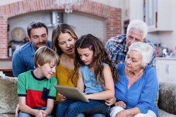 Multi-generation family sitting on sofa and using digital tablet