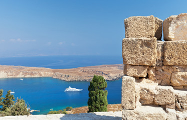 Detail of a stone wall of medieval fortress in Acropolis of Lindos on a background of blue sea, Rhodes, Greece