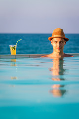 Fototapeta na wymiar Young Man Standing in Swimming Pool with Cocktail and looking at the Sea, Crete