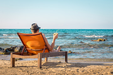 Young Man Relaxing on Chair Near the Sea and Drinking Cocktail Mojito