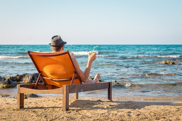 Young Man Relaxing on Chair Near the Sea and Drinking Cocktail Mojito