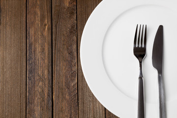 Fork and knife with white plate on dark wooden background, epty space on left - 109137567