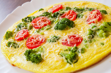 omelet with tomato, broccoli and cheese in a plate on wooden table