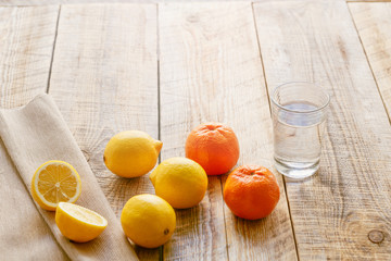 composition of lemons, oranges and glass with water  wooden table