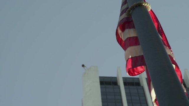 American flag weakly waving in the wind, a building with a prominent security camera on it in the background.