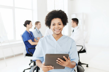 Obraz na płótnie Canvas happy nurse with tablet pc over team at hospital