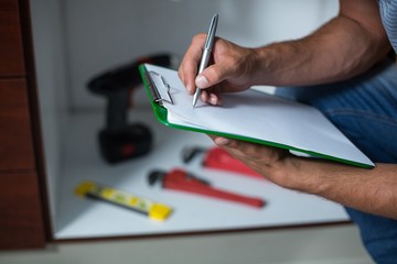 Midsection of man writing on clipboard 
