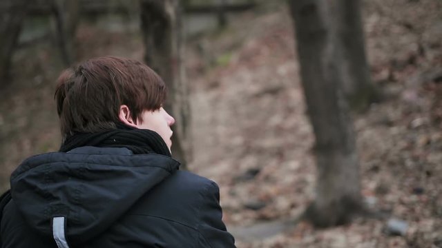 Back view of depressed young man sitting alone outdoors, having sad thoughts