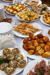 Catering banquet table with baked food snacks, sandwiches, cakes, cups and plates