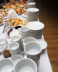 Catering banquet table with baked food snacks, sandwiches, cakes, cups and plates