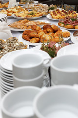 Catering banquet table with baked food snacks, sandwiches, cakes, cups and plates
