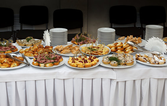 Catering banquet table with baked food snacks, sandwiches, cakes, cups and plates