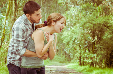 Young woman choking with man standing behind performing heimlich maneuver, park environment and...